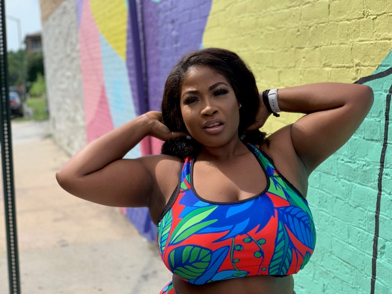 May include: A woman wearing a blue and red sports bra with a tropical leaf print. The bra has black straps and a black band around the bottom.