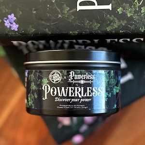 May include: A black round tin featuring the word "Powerless" in white script, with the text "Discover your power" beneath. The tin is adorned with green ivy and a white rim. The brand name "Wick Time" is also visible.