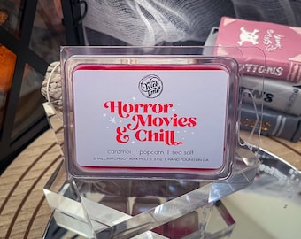 May include: A red wax melt in a clear plastic container with the text "Horror Movies & Chill". The label also lists caramel, popcorn, and sea salt scents. The wax melt is 85g and hand-poured in CA.