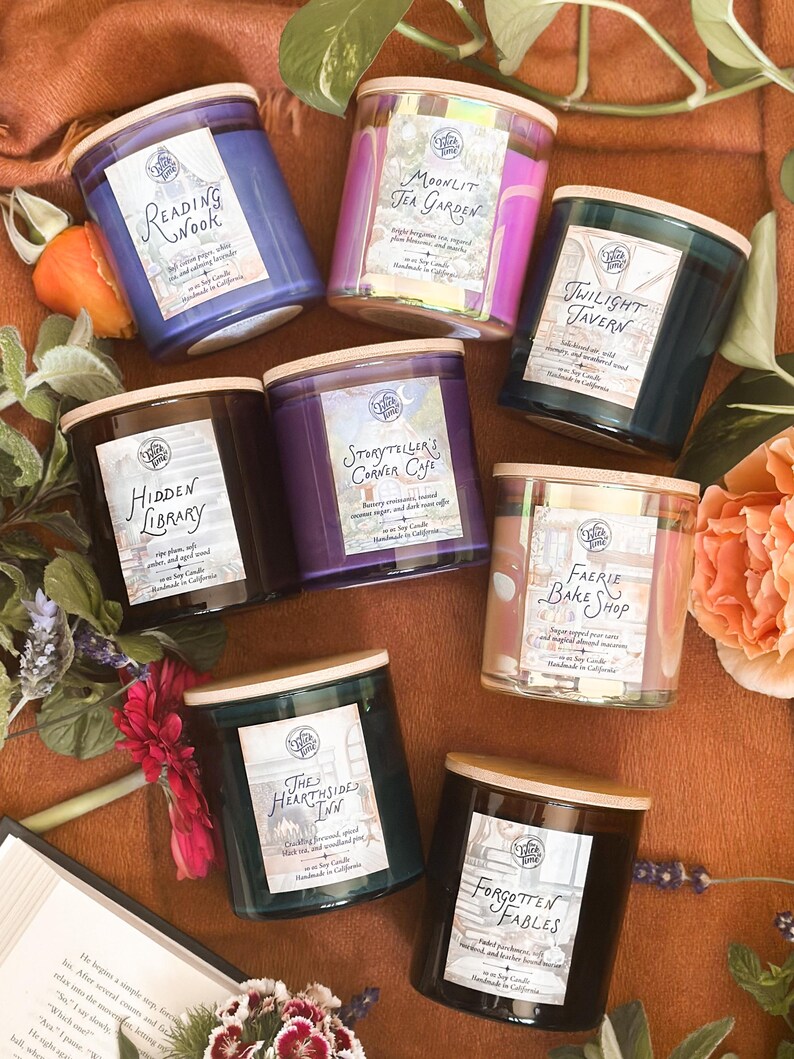 May include: An assortment of seven scented soy candles in glass jars with wooden lids. Each candle has a label with a unique name, such as "Reading Nook" and "Twilight Tavern." The candles are arranged on a brown surface with flowers and a book.