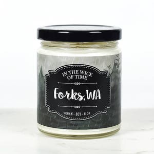 May include: A black and white candle jar with a label that reads "In the Wick of Time Forks, WA Vegan Soy 8 oz". The label has a black and white illustration of a forest with rain.
