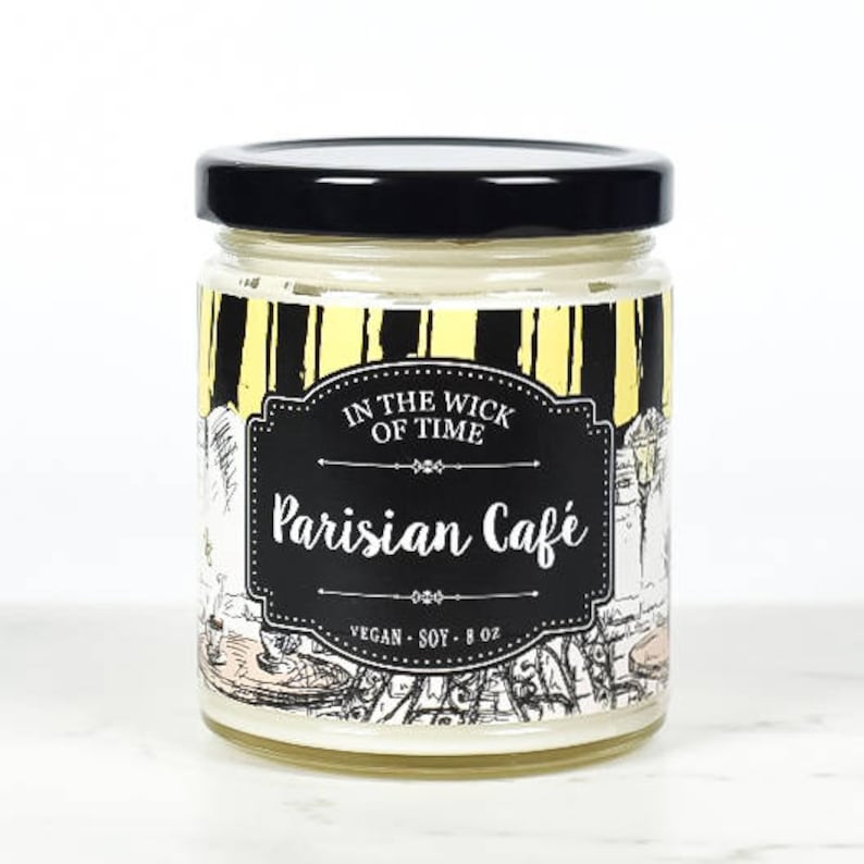 Puede incluir: Una vela en tarro de cristal con tapa negra. La etiqueta dice "In the Wick of Time Parisian Caf&eacute;" con un dise&ntilde;o en blanco y negro. La vela es vegana y de soja, y contiene 227 gramos.