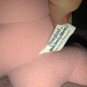 May include: Pink plush toy with a white tag that reads "Disneyland Walt Disney World Walt Disney Productions".