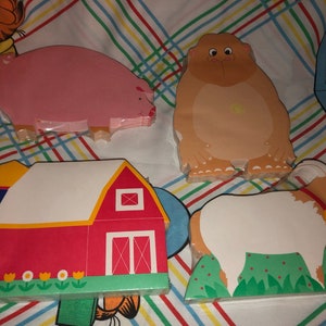 May include: Four colorful wooden animal shaped notepads. The notepads are shaped like a pig, a bear, a goat, and a barn. The notepads are all on a striped background.