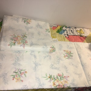 May include: White bed sheets with a floral pattern of pink, yellow, and green flowers and light blue leaves. The sheets are folded. The bedding is part of a set.