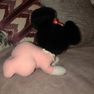 May include: A pink plush toy with black ears and a red bow. The toy is lying on its stomach with its head turned to the side.
