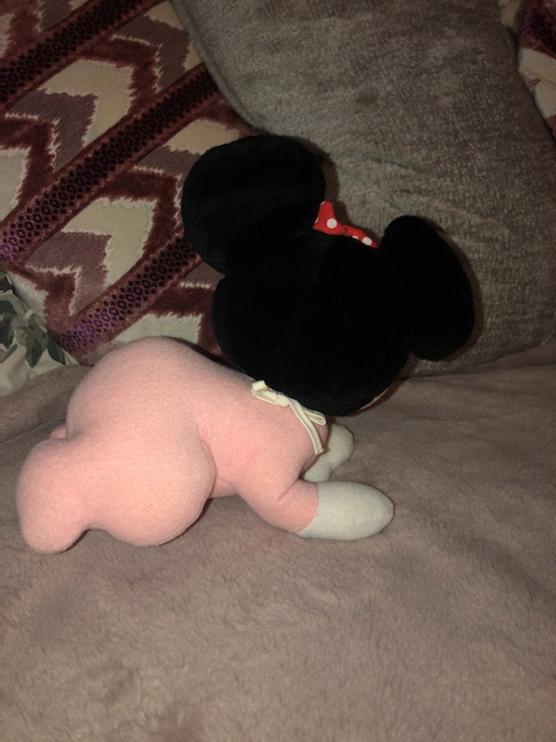 May include: A pink plush toy with black ears and a red bow. The toy is lying on its stomach with its head turned to the side.