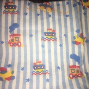May include: Blue and white striped fabric with a repeating pattern of yellow, red, and blue toy trains, aeroplanes, and boats. The fabric has a white background with blue stripes.