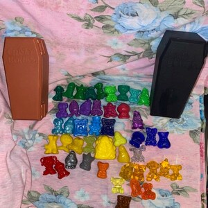 May include: A collection of colorful Crazy Bones figures and two coffin-shaped containers. The figures are in various colors, including green, purple, yellow, and orange. The brown container has the text "Crazy Bones" on it.