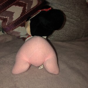 May include: Pink plush toy with a black head and a red bow. The toy is lying on a pink fuzzy blanket.