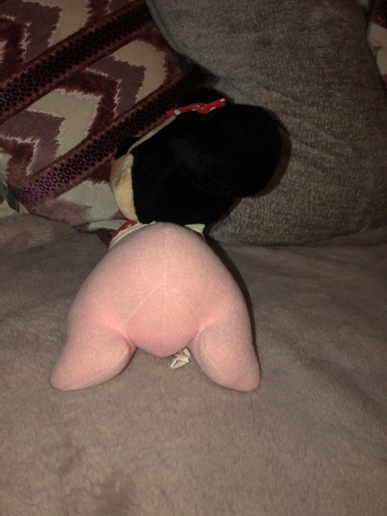 May include: Pink plush toy with a black head and a red bow. The toy is lying on a pink fuzzy blanket.