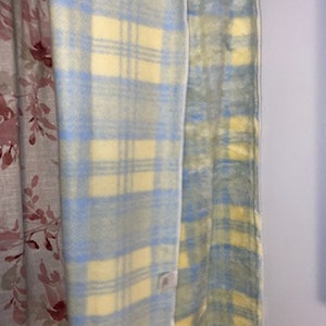May include: A blue and yellow plaid blanket with a white border. The blanket is folded in half and is hanging on a wall.