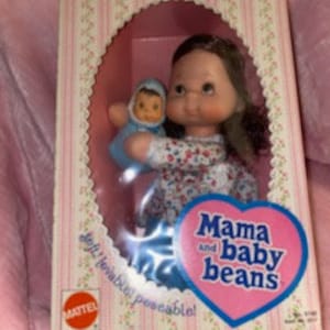 May include: Vintage Mattel Mama and Baby Beans doll set in original packaging. The doll is wearing a floral dress and holding a baby doll in a blue outfit. The box features the text "Mama and Baby Beans" and "soft, cuddly, poseable!"