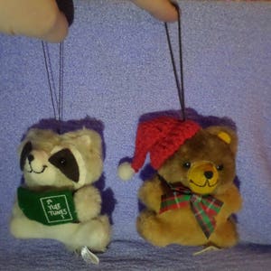 May include: Two plush Christmas ornaments, one is a raccoon wearing a green hat with the text "Yule Tunes" and the other is a brown bear wearing a red Santa hat.