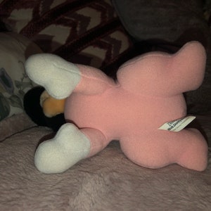 May include: Pink plush toy with white feet and a Disney Store tag. The toy is lying on its back with its legs in the air.