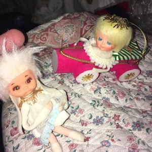 Peut inclure: Deux décorations de Noël vintage, l'une est une poupée blanche avec une robe bleue et l'autre est une poupée blonde dans une voiture rose.
