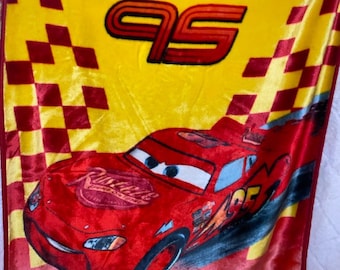 May include: A red and yellow fleece blanket featuring a red race car, the number 95, and the words "Lightning McQueen" and "Providencia".