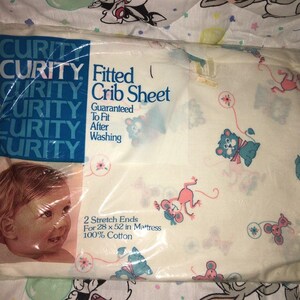 May include: A packaged Curity fitted crib sheet. The sheet is white with a pattern of cartoon animals in pink, blue, and green. The packaging includes the Curity logo and text that reads "Fitted Crib Sheet" and "Guaranteed To Fit After Washing."