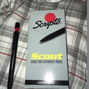 以下が含まれることがあります： 赤い消しゴムと銀色のクリップが付いた黒い機械式鉛筆。鉛筆には「Scripto Scout Ultra Thin Automatic Pencil 0.5mm Lead」とラベルが貼られています。