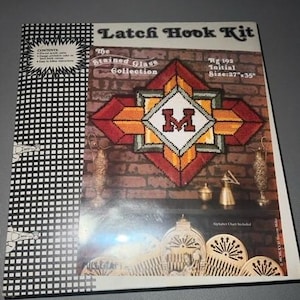 May include: Latch hook kit for a stained glass initial "M" in a red, orange, and yellow stained glass design. The kit includes an alphabet chart and is 27 inches by 35 inches.