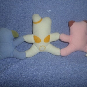 May include: Three plush toys, a blue one with ears, a white one with a yellow star and a pink one with brown ears.