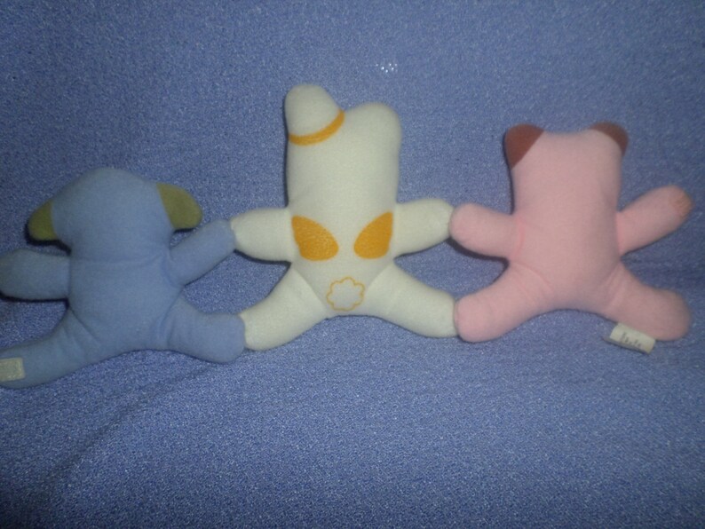 May include: Three plush toys, a blue one with ears, a white one with a yellow star and a pink one with brown ears.