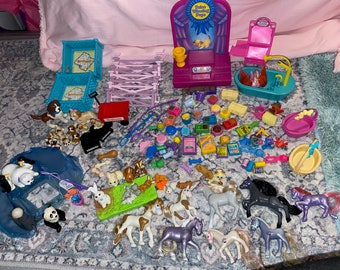 May include: A collection of miniature pet playset toys, including a blue and white playhouse, a pink grooming station, a blue bathtub, a pink and purple show ring, a red wagon, a blue and white dog kennel, a blue and white cat kennel, and a variety of animal figurines, including dogs, cats, horses, and a panda.