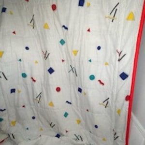 May include: White fleece blanket with a geometric pattern in red, blue, yellow, and green. The pattern includes circles, squares, triangles, and wavy lines.