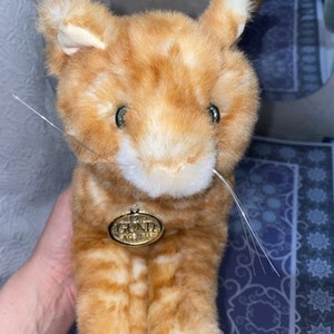 May include: Orange and white plush cat toy with a gold tag that says "GUND" on it.