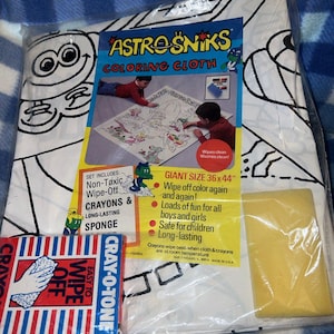 May include: Astro Sniks coloring cloth set, packaged in plastic. The set includes a giant 36x44 inch coloring cloth, non-toxic crayons, and a sponge. The packaging features the text "Wipe off color again and again!" and "Loads of fun for all boys and girls."