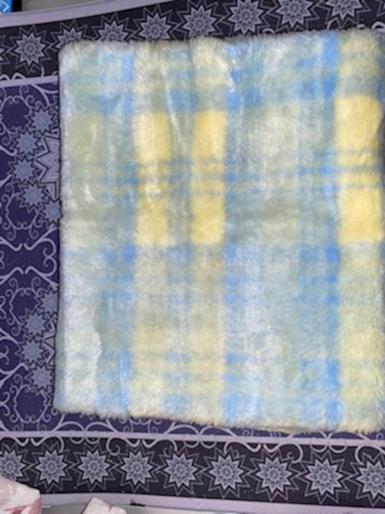 May include: A soft, fluffy rug with a blue and yellow plaid pattern. The rug is made of faux fur and has a light, airy feel.