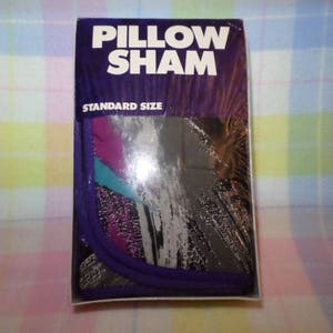 Puede incluir: Una caja de embalaje para una funda de almohada de tamaño estándar. La caja es morada y blanca con las palabras "Pillow Sham" en letras grandes, negritas y blancas. La caja tiene una ventana que muestra un diseño abstracto colorido en la funda de almohada.