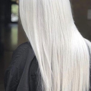 Könnte beinhalten: Langes, glattes, fließendes Haar in hellem Platinweiß. Das Haar fällt über den Rücken und kontrastiert mit einem schwarzen Kleidungsstück. Das Bild ist eine mittlere Aufnahme, die sich auf Textur und Farbe des Haares konzentriert.