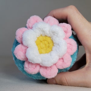 May include: A crocheted flower with pink, white and yellow petals. The flower is made of yarn and has a fuzzy texture.