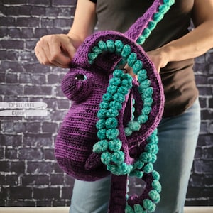 May include: A purple crochet octopus bag with teal accents. The bag features a detailed design with tentacles and a shoulder strap. The text "TopStitches Crochet" is visible on the left side of the image.