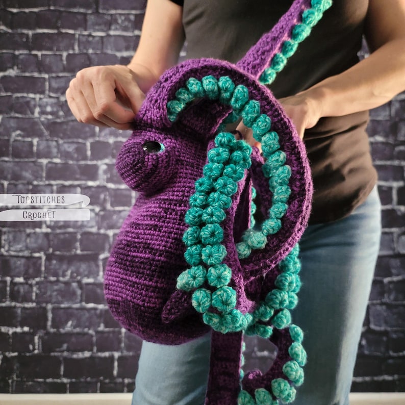 May include: A purple crochet octopus bag with teal accents. The bag features a detailed design with tentacles and a shoulder strap. The text "TopStitches Crochet" is visible on the left side of the image.