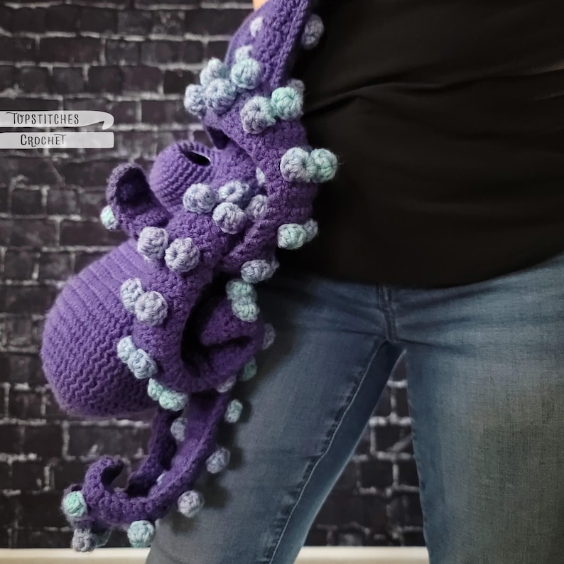May include: A purple crocheted octopus bag with light blue and purple bobbles. The bag has a round body and long tentacles. The text "Topstitches Crochet" is visible on the left side of the image.