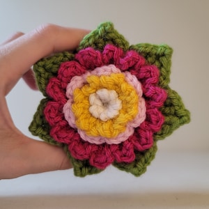 Può includere: Un fiore all'uncinetto con petali verdi, rosa, gialli e bianchi.