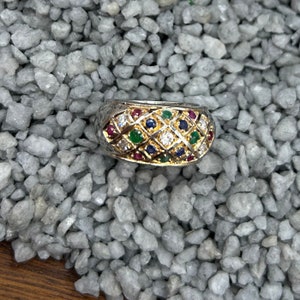 Könnte beinhalten: Ein silberner Ring mit einem goldenen Band, besetzt mit Diamanten und bunten Edelsteinen, darunter Smaragde, Rubine und Saphire.