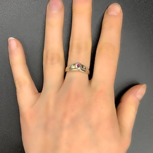 Peut inclure: Une bague en or avec une pierre précieuse rouge et de plus petites pierres blanches. La bague est portée sur un doigt.