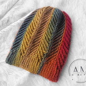 Könnte beinhalten: Eine bunte Häkelmütze mit Chevron-Muster in Blautönen, Grün, Braun, Orange und Rot. Die Mütze liegt auf einer weißen, flauschigen Oberfläche.