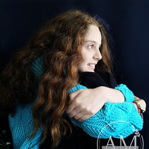 Puede incluir: Una mujer con el pelo largo y castaño lleva un top de ganchillo azul y una camisa negra. Se está abrazando y mirando hacia un lado. La imagen incluye el texto "AM - crochet designs - ".