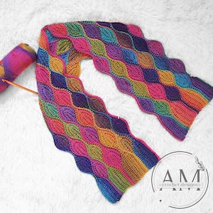 Può includere: Una sciarpa all'uncinetto colorata con un motivo ondulato in tonalità di rosa, viola, blu, verde e arancio. La sciarpa è realizzata con un filato variegato e presenta un design testurizzato unico.