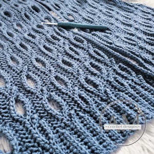 Puede incluir: Un primer plano de una tela de crochet azul con un patrón repetitivo de agujeros. La tela es texturizada y tiene un aspecto suave y peludo. El texto "AM - crochet designs -" es visible en la esquina inferior derecha de la imagen.