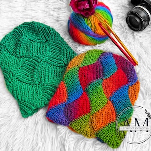May include: Two handmade knit beanies in the image. One is solid green, the other is a patchwork of rainbow colors. A ball of rainbow yarn, crochet hooks, and a camera are also in the image. The beanies are on a white, fluffy surface.