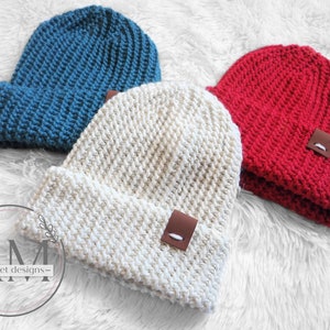 May include: Three crocheted beanies in different colors: teal, cream, and red. Each beanie has a brown leather patch with a white stitch detail.
