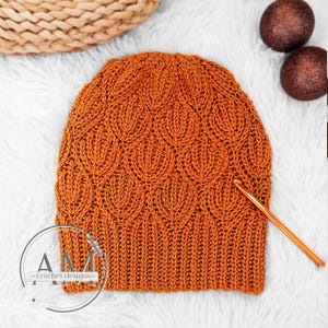 Puede incluir: Un gorro de punto de ganchillo de color naranja cálido con un patrón de hojas texturizado. El gorro está hecho con punto bajo y tiene un borde de canalé.