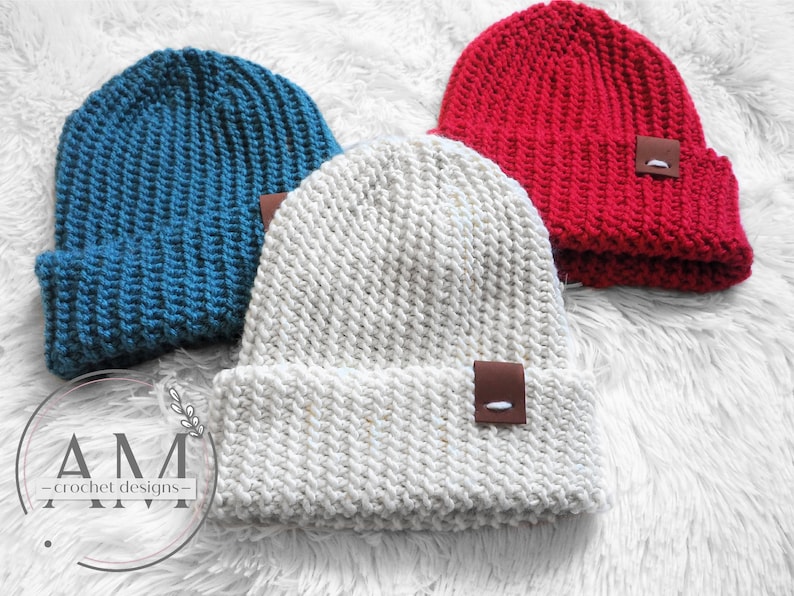 May include: Three crocheted beanies in different colors: teal, white with flecks of gold, and red. Each beanie has a brown leather patch with a white stitch detail.