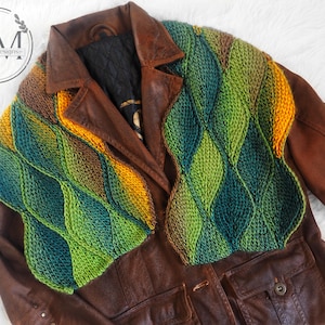 May include: A brown leather jacket with a green, blue, and yellow crocheted scarf. The scarf has a diamond pattern.