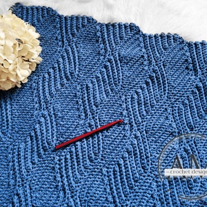 Könnte beinhalten: Eine blaue Häkeldecke mit einem strukturierten Muster. Eine rote Häkelnadel liegt auf der Decke. Die Decke ist aus einem dicken Garn gefertigt und fühlt sich weich und gemütlich an.